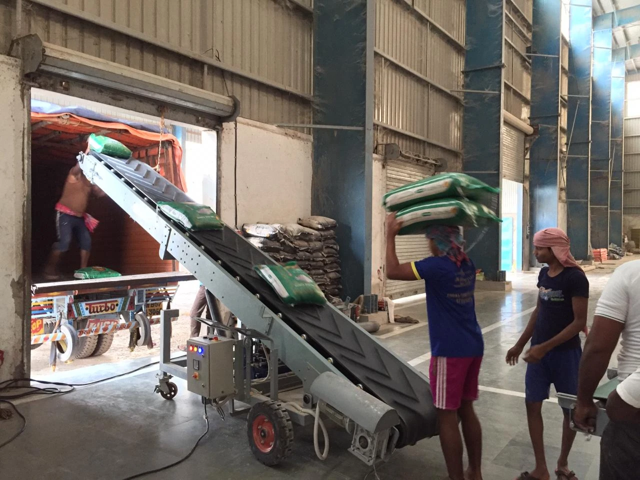 Labours are loading products into truck with the help of truck loading conveyor